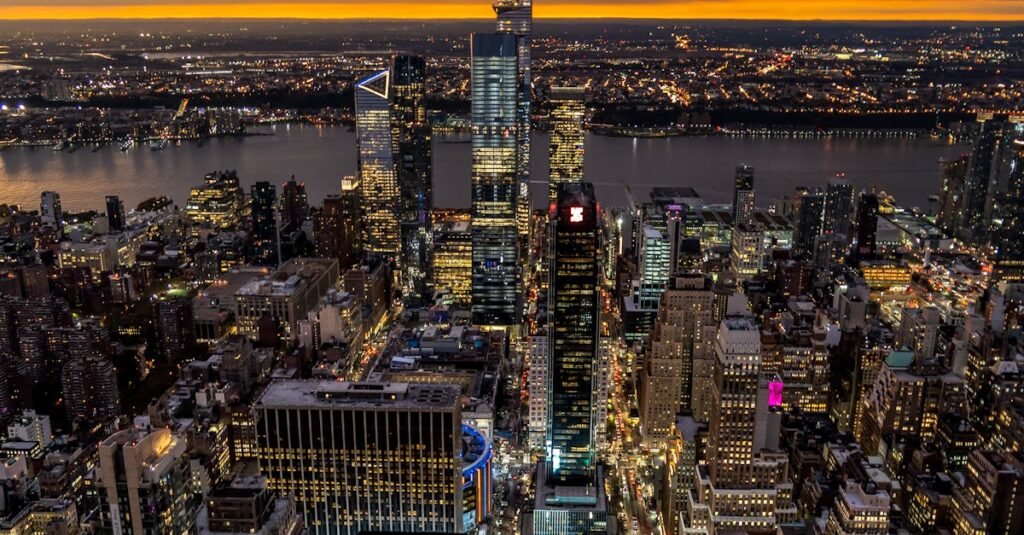 Aerial view of New York City's vibrant skyline during dusk with dramatic clouds and city lights.